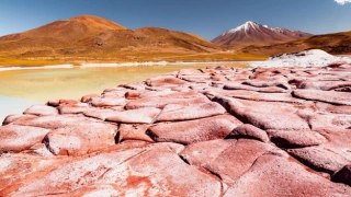 Foco em grandes pedras planas de cor avermelhada no plano frontal. Ao fundo, um lago e montanhas vulcânicas