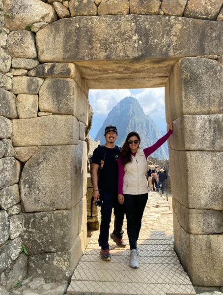 Homem e mulher posando para foto debaixo de um portal feito em pedra em Machu Picchu, Peru.