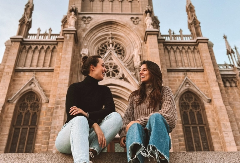 Duas mulheres conversando sentadas em frente a igreja com arquitetura imperial