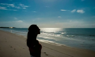 Mulher contempla paisagem de praia deserta olhando em direção ao céu azul