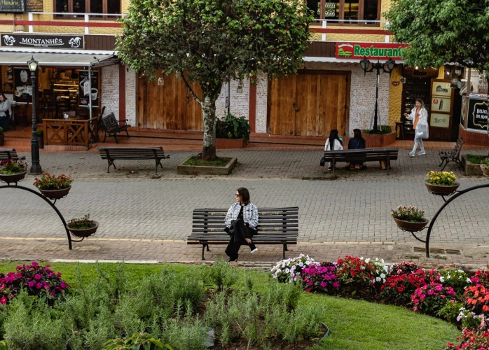 Mulher sentada em banco de praça em meio à cidade pacata.