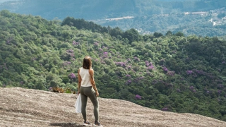 No alto de uma grande pedra, mulher observa a natureza.