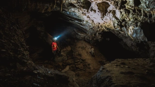 Homem de capacete com lanterna em pé em meio às estruturas de uma caverna escura