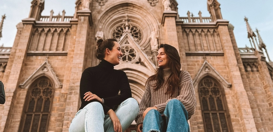 Duas mulheres conversando sentadas em frente a igreja com arquitetura imperial