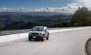 Jeep Renegade em movimento em uma estrada com montanhas verdes e um céu azul atrás.