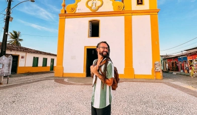 Gabriel Elias sorrindo em frente à capela de arquitetura colonial em dia ensolarado