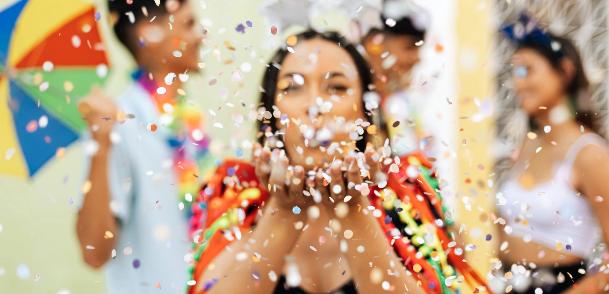 Mulher soprando confetes de papel no Carnaval no Brasil. Há mais três pessoas ao fundo, todas desfocadas