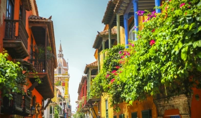 Rua com casas coloridas na Colômbia, algumas com plantas em suas varandas e catedral ao fundo