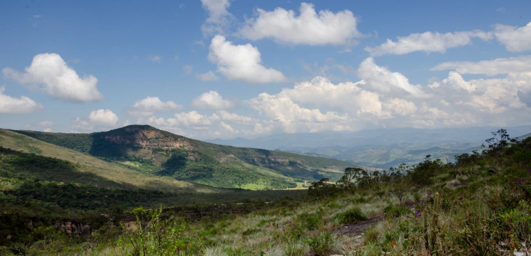 Vista para uma montanha coberta por vegetação em dia ensolarado com poucas nuvens