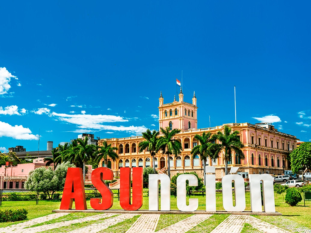 Destaque para letreiro escrito “Asunción”. Ao fundo está o grande palácio que é sede do governo