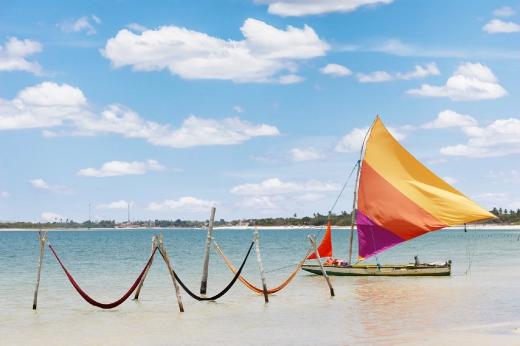Vela de barco e redes em Jericoacoara, Brasil, em um dia ensolarado. A vela tem as cores amarelo, laranja e roxo.