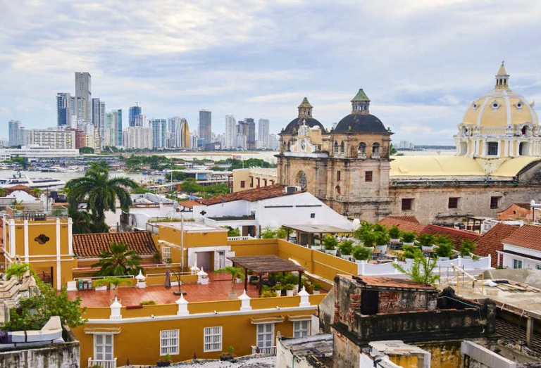 Vista aérea da cidade de Cartagena. No plano frontal, construções coloniais com cores vibrantes. Ao fundo, prédios altos e modernos.
