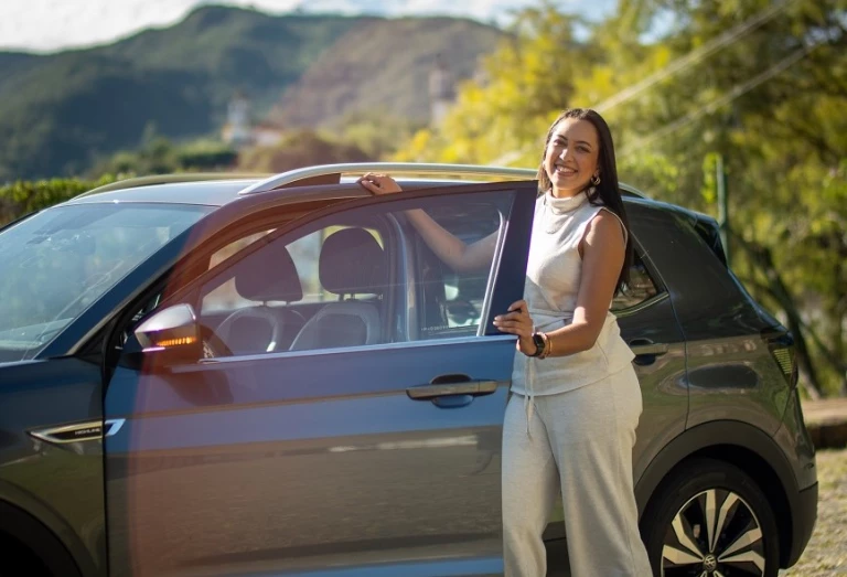Mulher posa ao lado de carro estacionando em rua em um dia claro