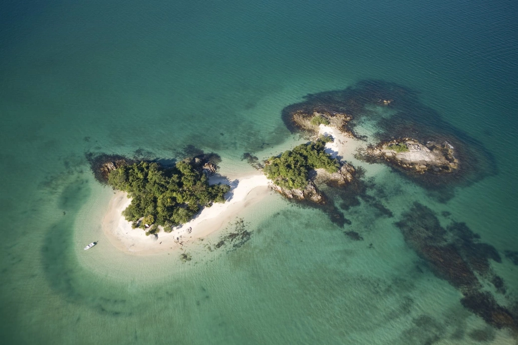 Vista aérea de uma ilha com cobertura vegetal, cercada por mar de coloração verde-esmeralda