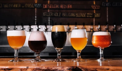 Vários copos de cerveja artesanal de diferentes cores sob um balcão de um bar