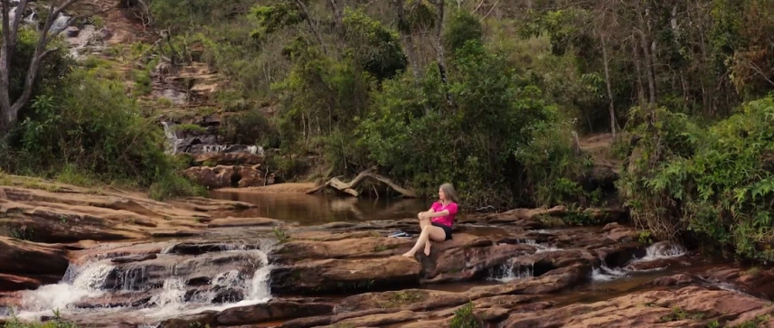 Mulher sentada em pedra de cachoeira contempla águas claras
