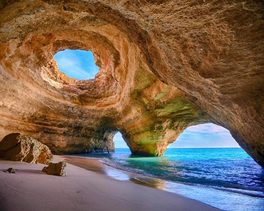 Gruta de Benagil, em Algarve, Portugal. A caverna possui um buraco redondo no teto, por onde entra a luz do sol, além de duas aberturas em formato de arco que permitem a passagem da água do mar.