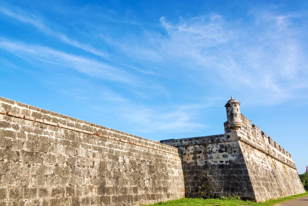 Muralha antiga de pedra na cidade de Cartagena, Colômbia, com céu azul e poucas nuvens ao fundo.