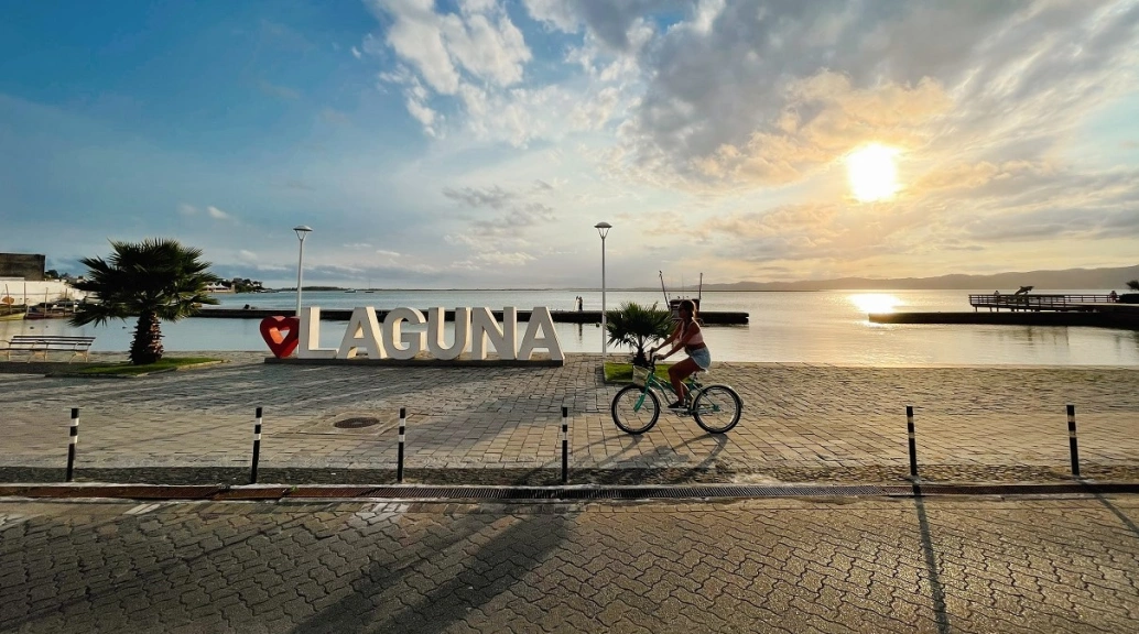 Mulher andando de bicicleta em calçada à beira-mar em dia ensolarado