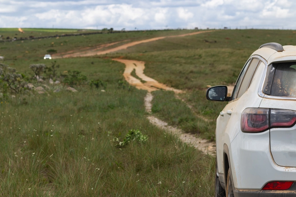 Vista da traseira de um carro branco seguindo pela estrada de terra da Serra da Canastra em dia ensolarado.