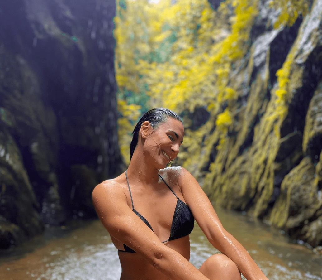 Close em mulher sorridente que pratica atividade aquática em uma abertura que origina uma piscina natural em meio à natureza.