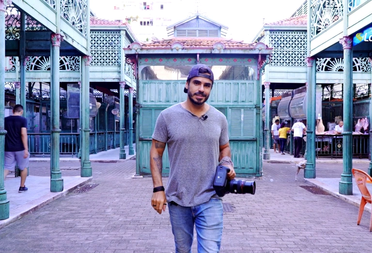 Fotógrafo Ricardo Martins caminha por feira segurando câmera em dia claro