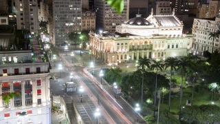 Vista aérea de uma avenida com ruas asfaltadas e vários prédios ao redor com luzes da avenida acesas devido a chegada da noite.