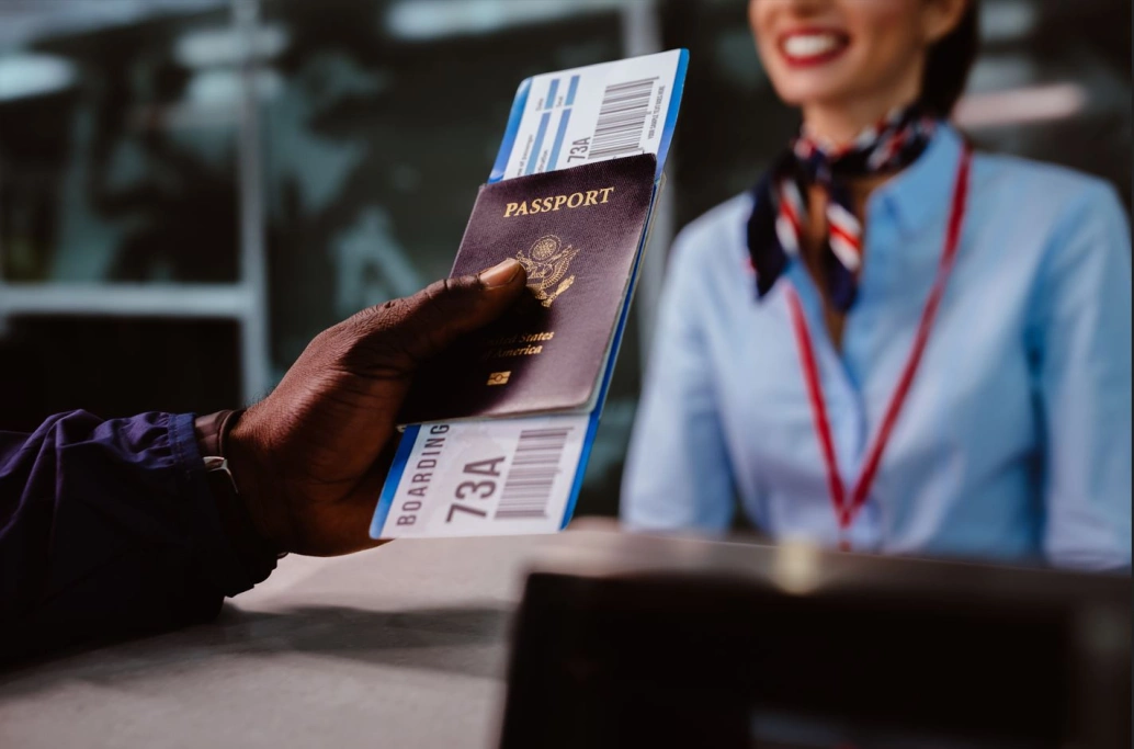 Mão de uma pessoa entregando um passaporte e uma passagem aérea a uma atendente do aeroporto