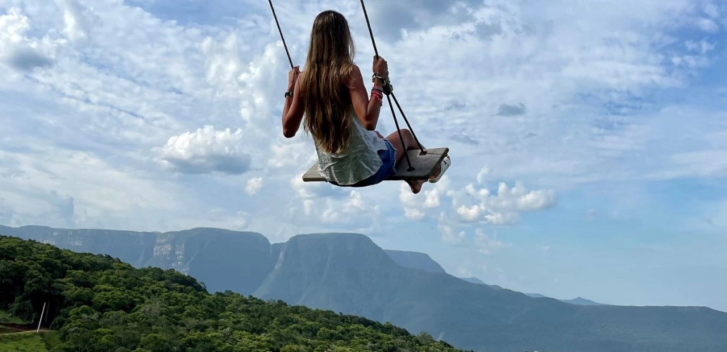 Mulher brinca em balanço de frente para paisagem de montanhas e árvores