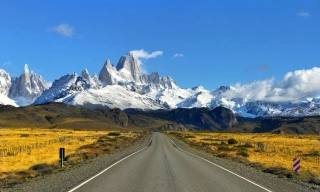 Vista de estrada asfaltada em meio a Argentina. Ao fundo, montanhas enevoadas em dia claro