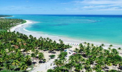 Vista aérea de praia em São Miguel dos Milagres, Alagoas. O azul reluzente do lar contrasta com a areia branca e vegetação exuberante.