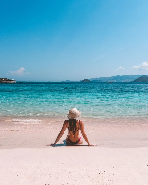 Mulher de costas para a câmera sentada na areia de uma praia paradisíaca da Indonésia