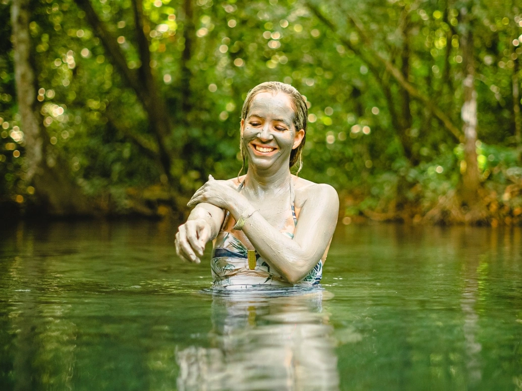 Mulher passa argila sobre a pele tomando banho em lagoa Refúgio Água Azul em Nobres