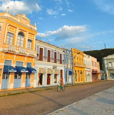 Mulher anda de bicicleta em ruas de cidade histórica com casas de fachadas coloridas
