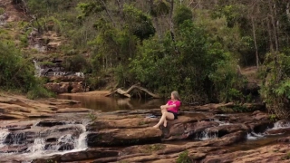 Mulher sentada em pedra de cachoeira contempla águas claras