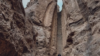 Homem posando para foto na base de uma cachoeira seca que fica entre uma formação rochosa bem alta