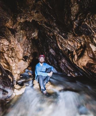 Homem usando equipamentos de proteção individual sentado no interior de uma gruta.